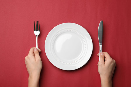 Woman with fork, knife and empty plate on color background, top viewの写真素材