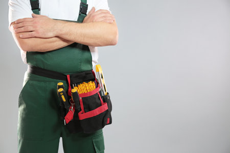 Professional construction worker with tool belt on gray background, closeup. Space for textの写真素材