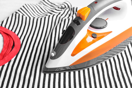 Modern electric iron and wrinkled t-shirt on table, closeup. Space for textの写真素材
