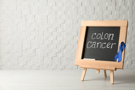 Chalkboard with blue ribbon and text Colon cancer awareness on tableの写真素材
