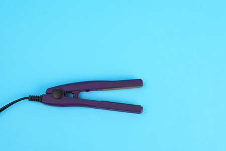 Modern hair iron for straightening on color background, top view