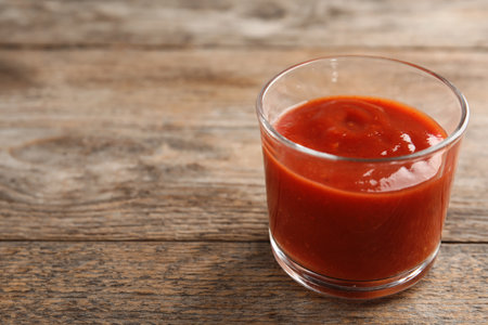 Glass of tasty tomato sauce on wooden table. Space for textの写真素材