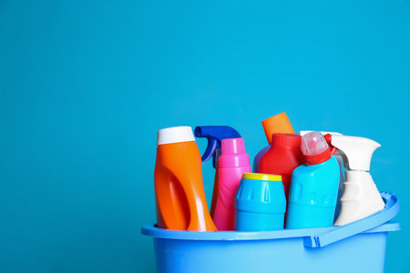 Plastic bucket with different cleaning products against color background. Space for textの写真素材