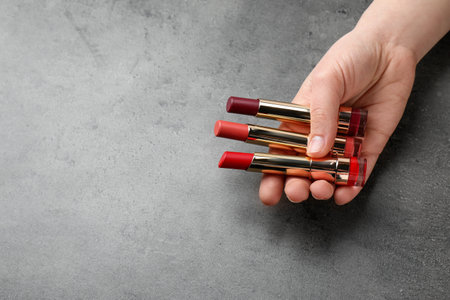 Woman holding different lipsticks on color background, closeup with space for text. professional makeup productsの写真素材