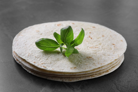Stack of tasty tortillas with basil leaves on gray table, closeupの写真素材