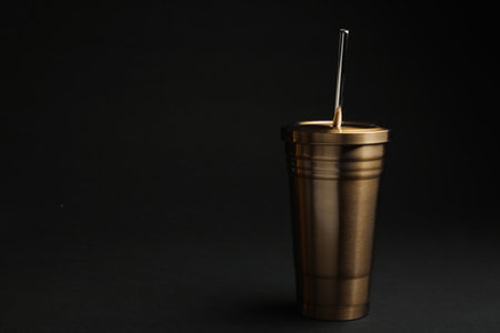 Gold cup with straw on black background. Space for textの写真素材