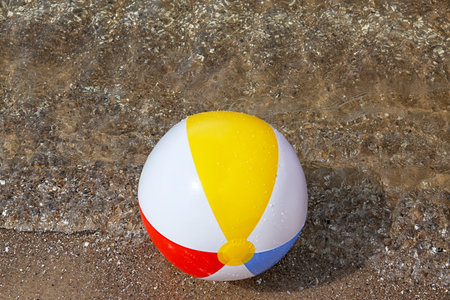 Bright inflatable beach ball on sandy beach near seaの写真素材