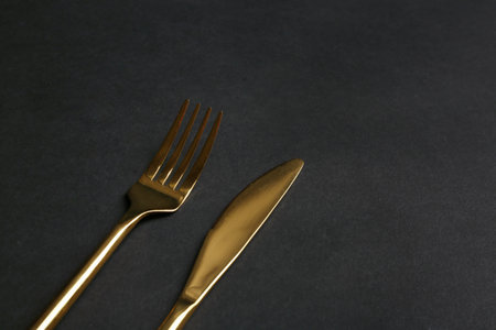 Gold fork and knife on black background. Space for textの写真素材