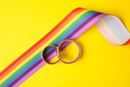 Wedding rings and rainbow ribbon on color background, top view. gay symbolの写真素材