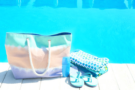Beach accessories on wooden deck near swimming pool. Space for text