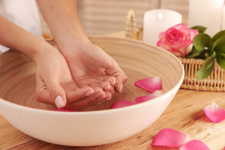 Woman soaking her hands in bowl with water and petals on table, closeup. spa treatmentの写真素材