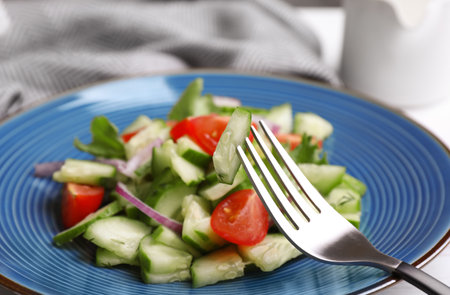Delicious fresh cucumber tomato salad and fork on table, closeupの写真素材