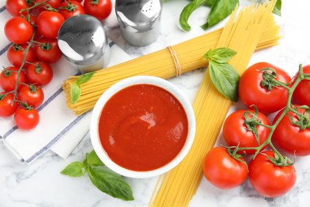 Flat lay composition with bowl of sauce, pasta and tomatoes on marble table