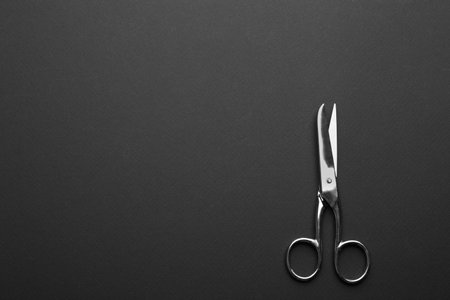 Pair of sharp scissors on dark background, top view. Space for text