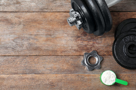 Flat lay composition with protein powder and dumbbell on wooden background. Space for textの写真素材