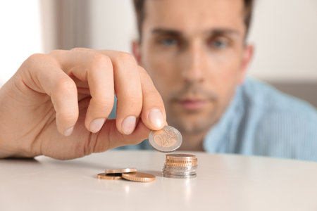 Young man stacking coins at table, focus on handの写真素材