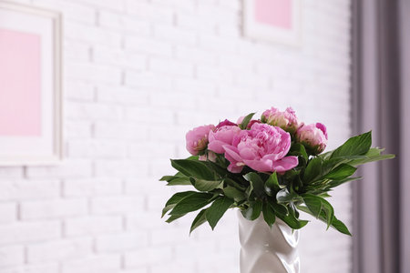Vase with bouquet of beautiful peonies at white wall in room, space for textの写真素材
