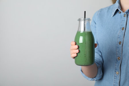 Woman holding bottle with spirulina smoothie on gray background, closeup. Space for textの写真素材