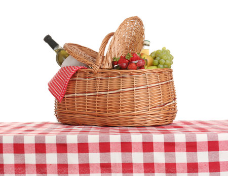 Picnic basket with wine and fruits on tablecloth against white backgroundの写真素材