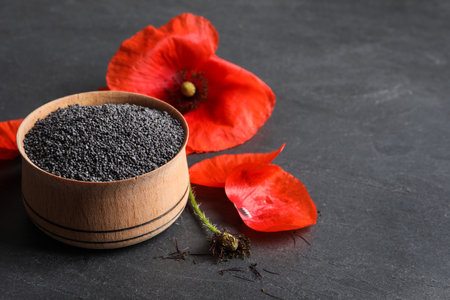 Wooden bowl of poppy seeds and flower on gray table, space for textの写真素材