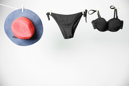 Stylish bikini and hat hanging on rope against light backgroundの写真素材