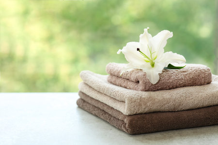 Stack of clean towels with lily on table against blurred background. Space for textの写真素材
