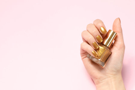 Woman holding bottle of golden nail polish in manicured hand on color background, top view. Space for textの写真素材