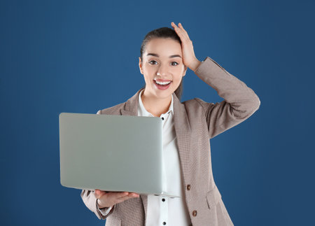 Portrait of happy young woman in office wear with laptop on color backgroundの写真素材