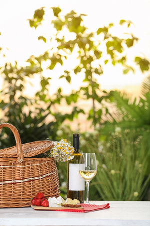 Picnic basket and wine with products on table against blurred background, space for textの写真素材