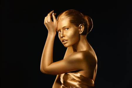 Portrait of beautiful lady with gold paint on skin against black backgroundの写真素材