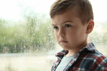 Cute little boy near window indoors, space for text. rainy dayの写真素材