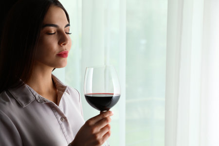 Beautiful young woman with glass of luxury red wine indoors. Space for textの写真素材