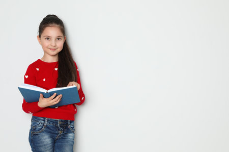 Cute little girl reading book on white background, space for textの写真素材