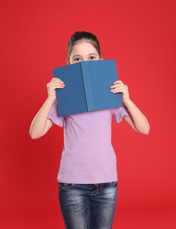 Cute little girl hiding behind book on color background. Reading activityの写真素材