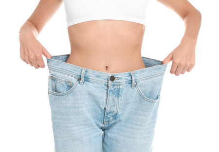 Slim young woman with smooth gentle skin in oversized jeans on white background, closeup. beauty and body care conceptの写真素材
