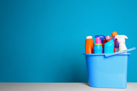 Plastic bucket with different cleaning products on table against color background. Space for textの写真素材