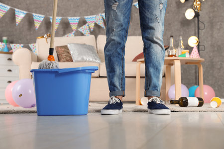 Man with mop and bucket cleaning messy room after party, closeup view of legsの写真素材