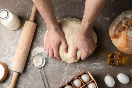 Male baker preparing bread dough at kitchen table, top view