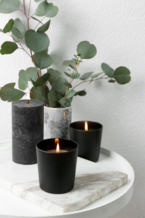 Burning candles and green branches on table at white wall, space for textの写真素材