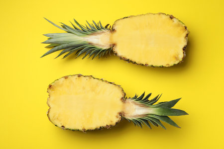 Halves of fresh pineapple on yellow background, top view
