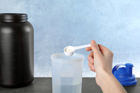 Man preparing protein shake with powder at table, closeup