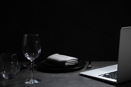 Composition with tableware and laptop on table against black background, space for text. Loneliness conceptの写真素材