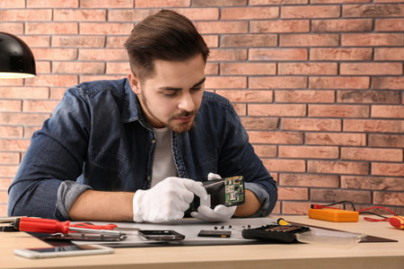 Technician repairing broken smartphone at table in workshop. Space for textの写真素材