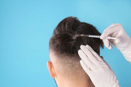Young man with hair loss receiving problem injection on color background. Space for textの写真素材
