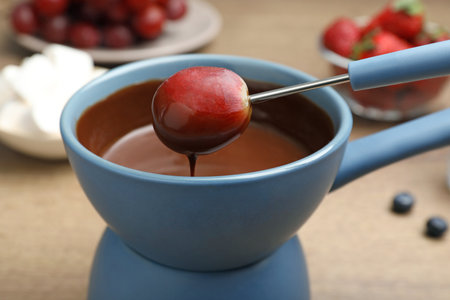 Dipping grape into pot with chocolate fondue on table, closeupの写真素材