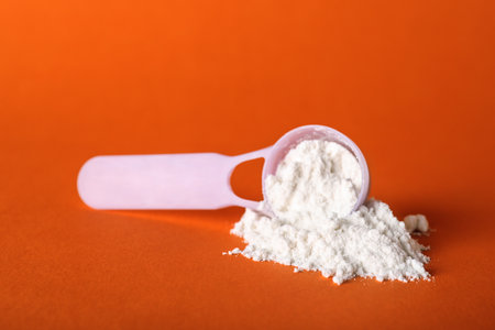 Scoop and scattered protein powder on orange background