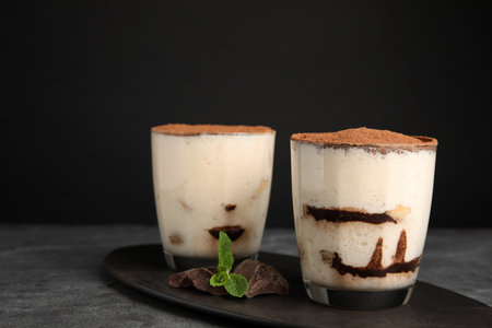 Two glasses of tiramisu cake on table against dark background, space for textの写真素材