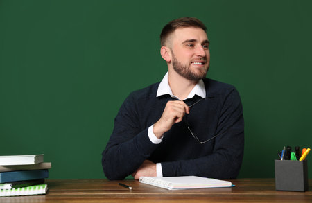 Portrait of young teacher at table against green background. Space for textの写真素材