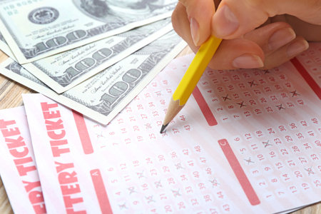 Woman filling out lottery tickets with pencil and money on wooden table, closeup. Space for textの写真素材