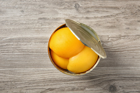 Open tin can of peaches on wooden background, top viewの写真素材